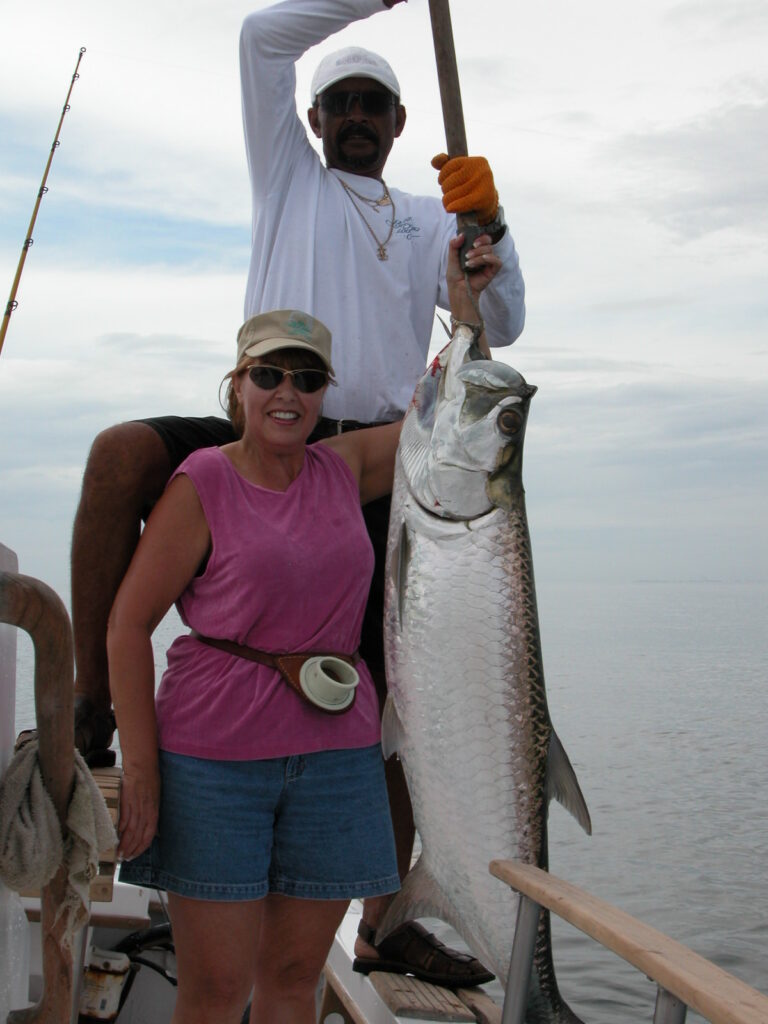 Female angler posing with a trophy tarpon fish held vertically by a guide during a guided tarpon fishing trip in Costa Rica.