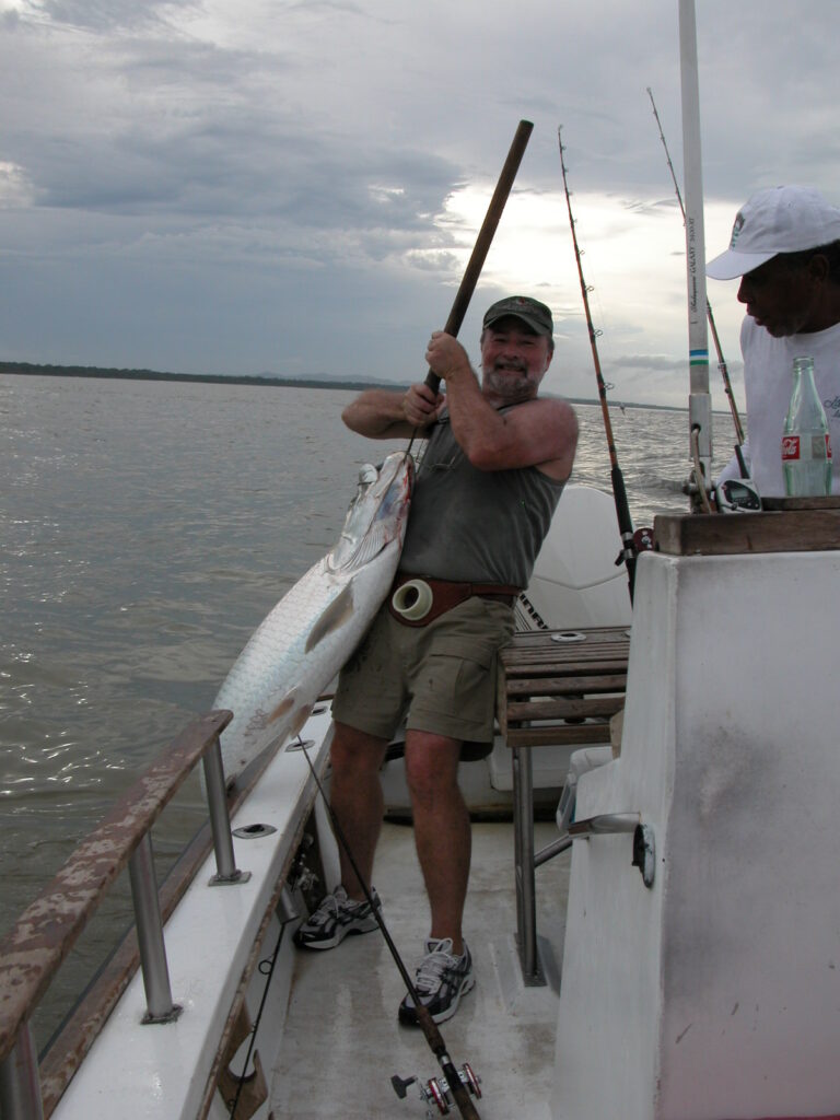 Kraken Founder, Bob Kern, lifting a large tarpon fish on a boat under overcast skies during a guided tarpon fishing trip in Costa Rica.